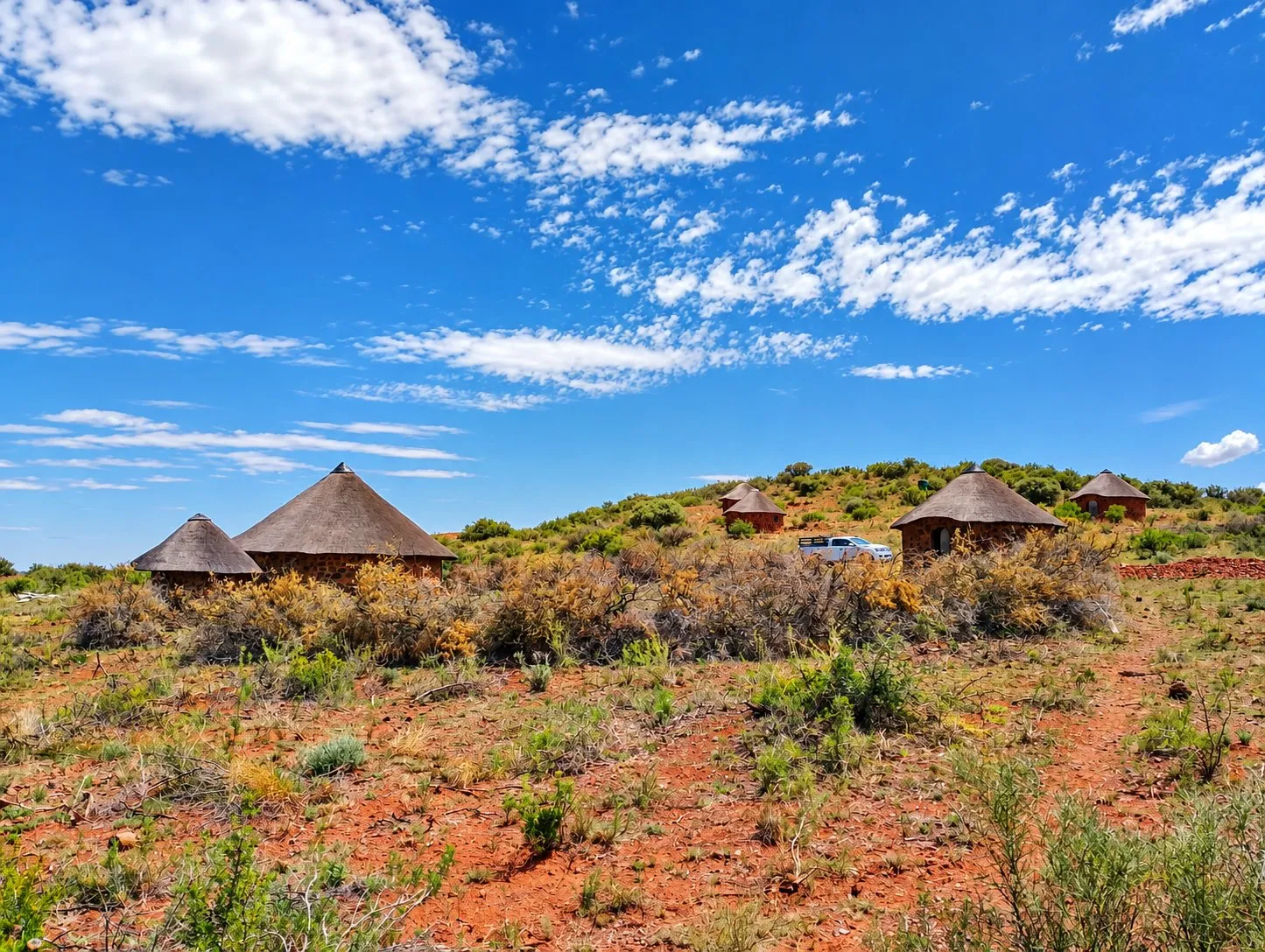 Thatched rondavels on a bush covered hillside under a bright blue sky.