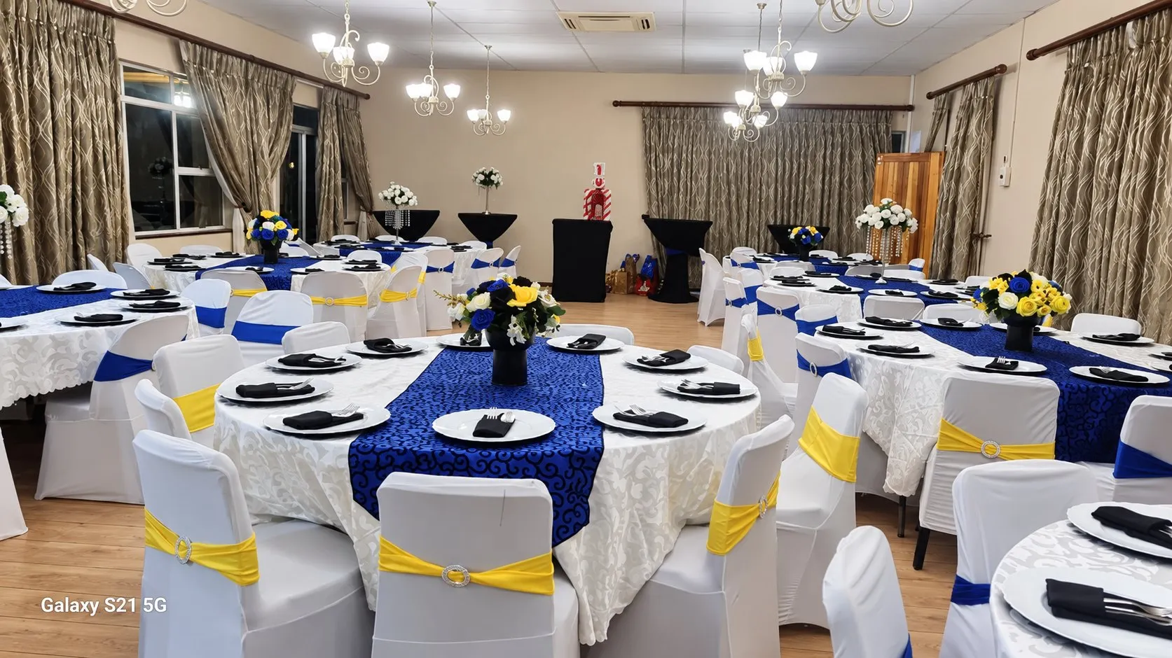The function hall set with round tables in white and royal blue under chandeliers.