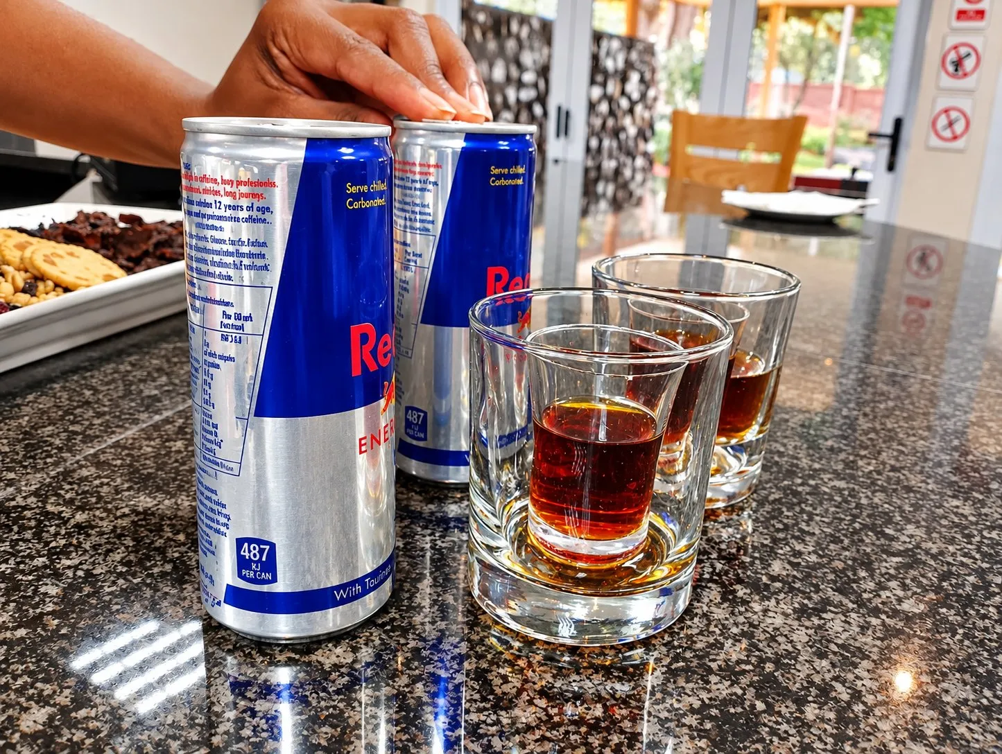 Two cans of energy drink and shot glasses of an amber spirit on the granite bar counter.